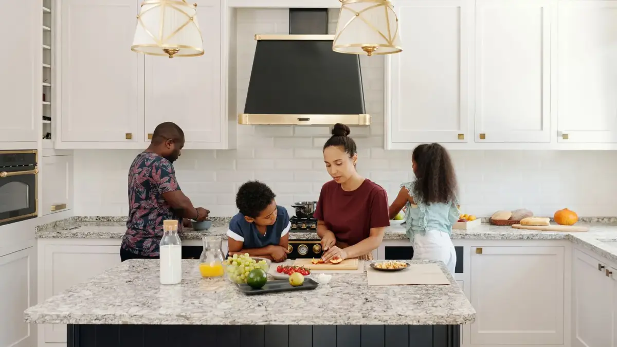 A family of four preparing a meal together at a kitchen island in a bright white kitchen