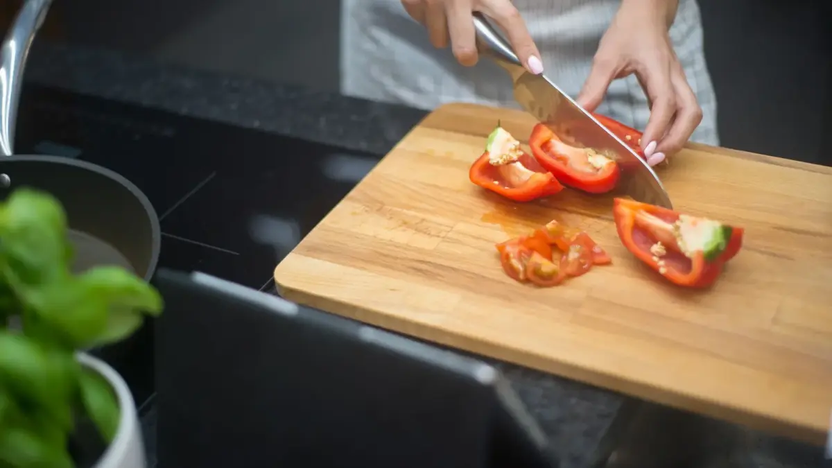 Hands slicing a red bell pepper on a wooden chopping board