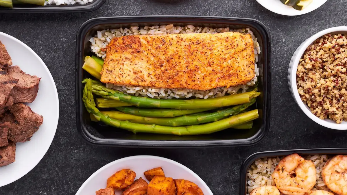 Overhead view of meal-prep containers and bowls with salmon, asparagus, shrimp, sweet potatoes and rice