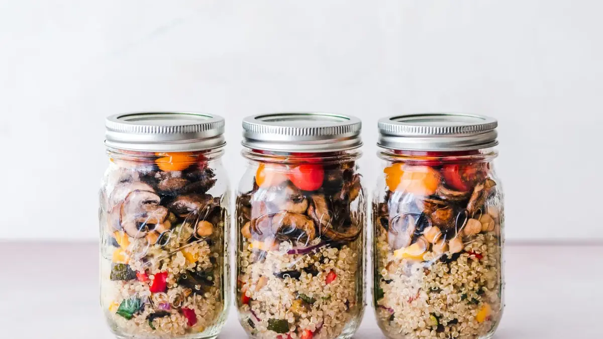 Three glass jars of quinoa salad with roasted vegetables lined up on a white surface