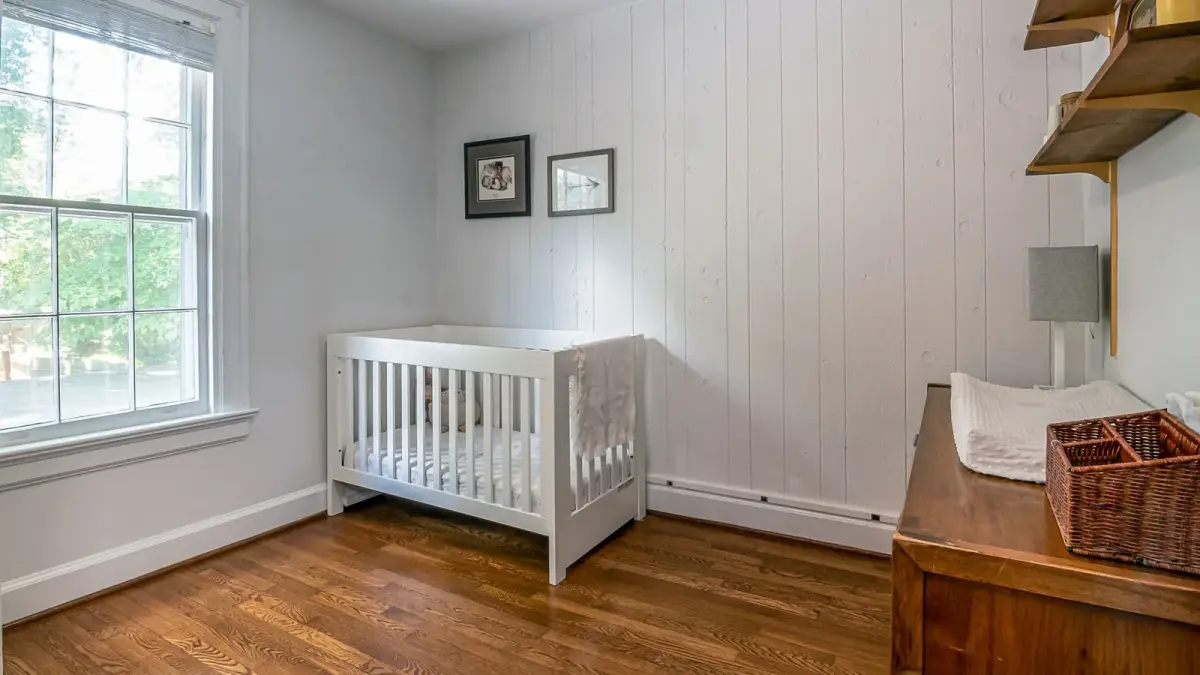 A bright nursery with a white wooden crib beside a window and a changing table