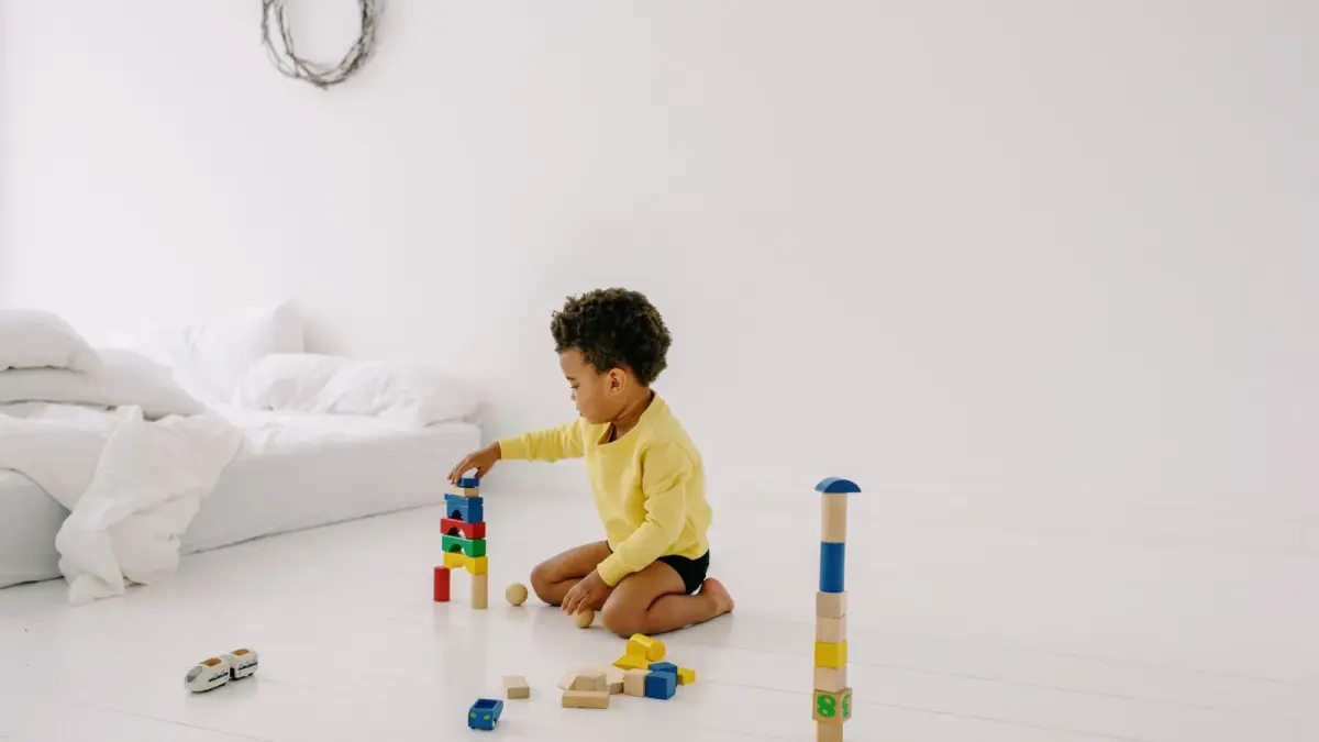 A toddler playing with colorful wooden blocks on a white bedroom floor